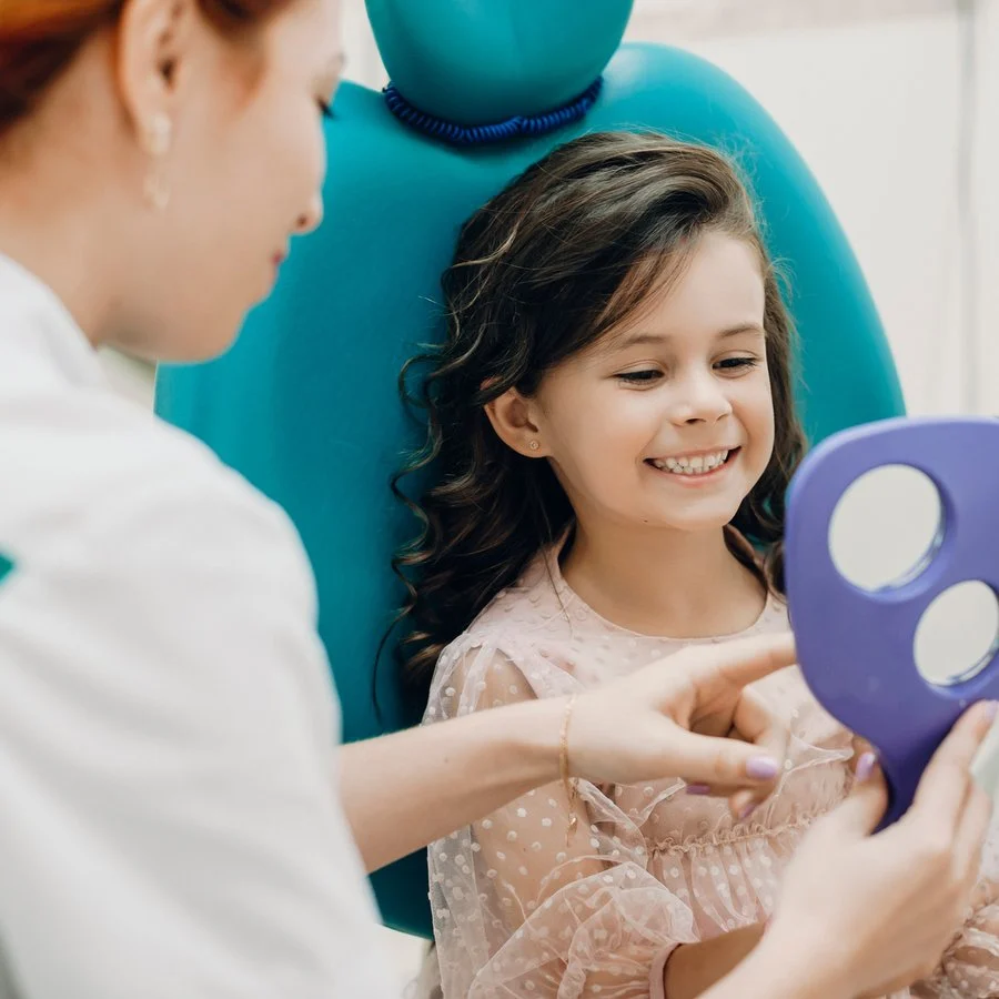Young girl smiling while looking in a mirror at the dentist