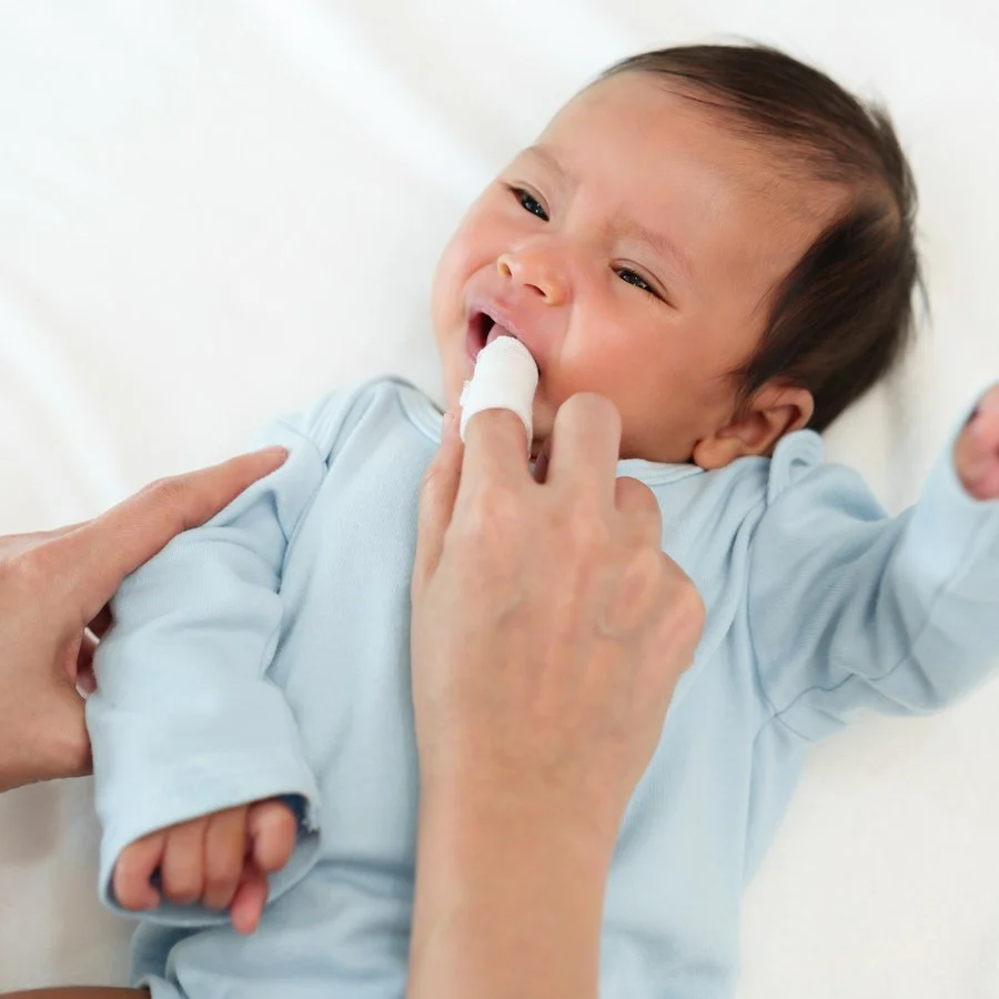Mother gently cleaning her baby’s gums with a clean gauze