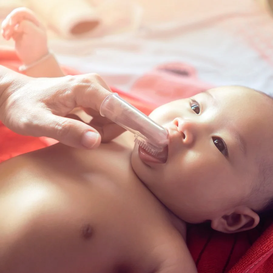 Mother using a finger toothbrush to clean her baby’s mouth