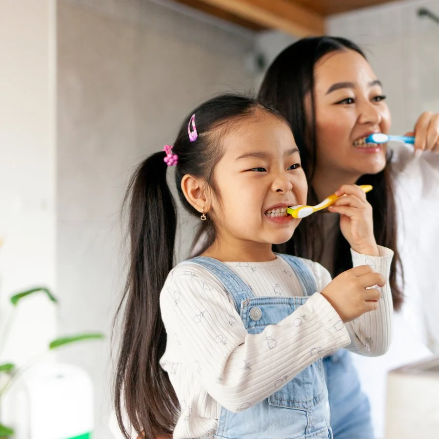 Mother helping her young daughter brush her teeth