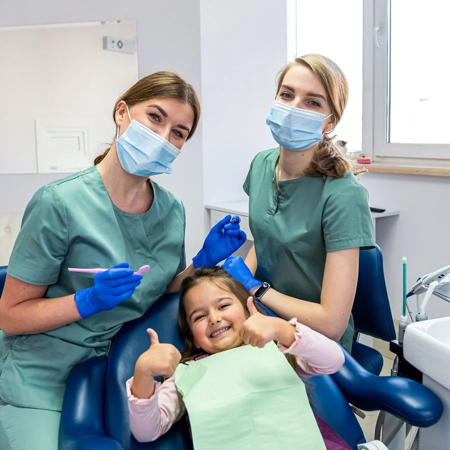 Pediatric dentist and assistant with a smiling child giving a thumbs up
